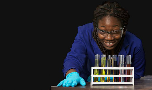 A female apprentice leans over some test tubes.